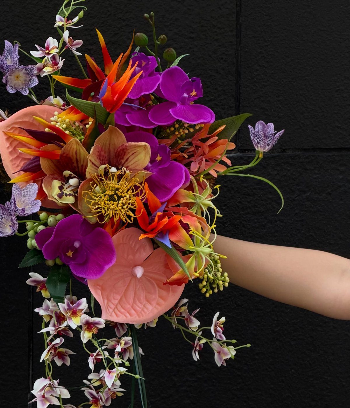 Tropical bouquet with purple orchids and orange bird of paradise held against black background