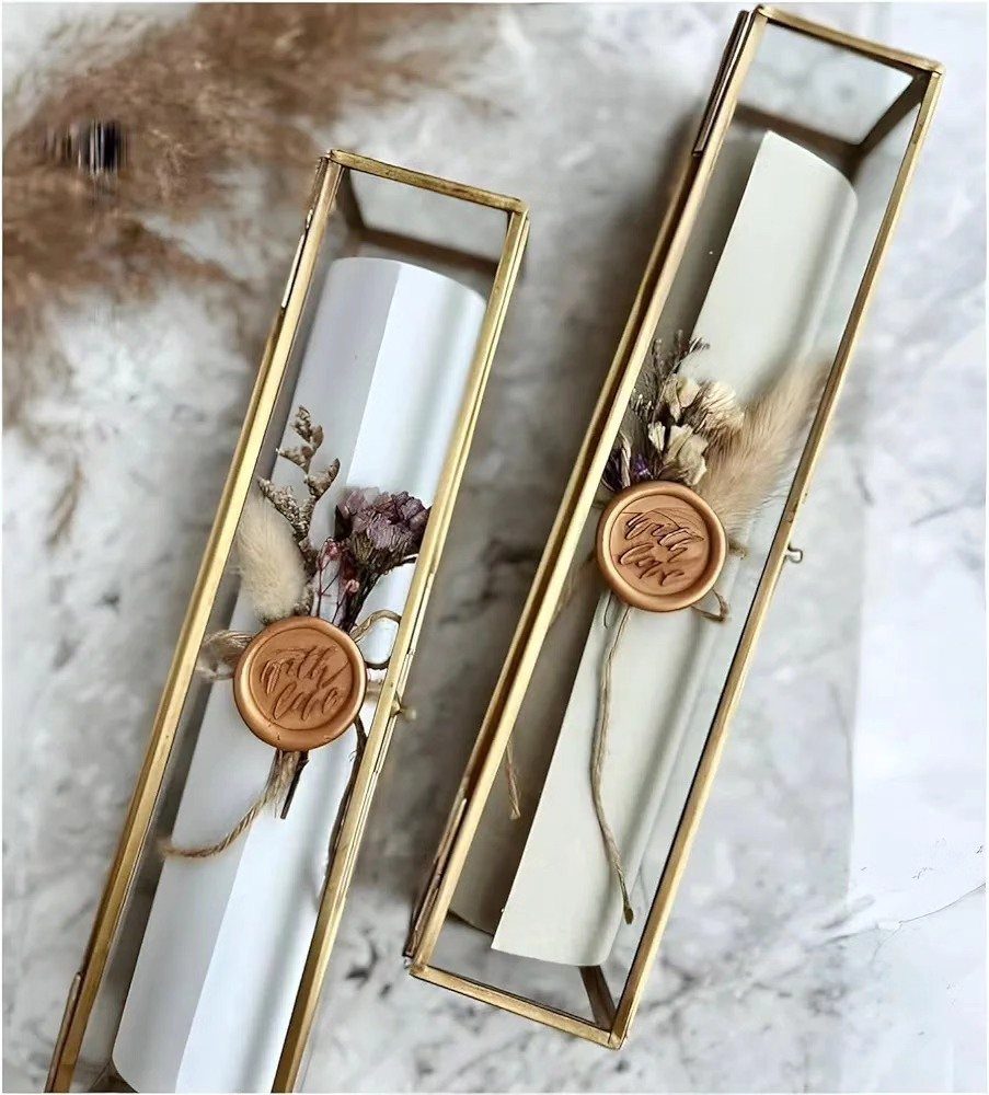 Two glass boxes with gold frames containing rolled scrolls and dried flowers.