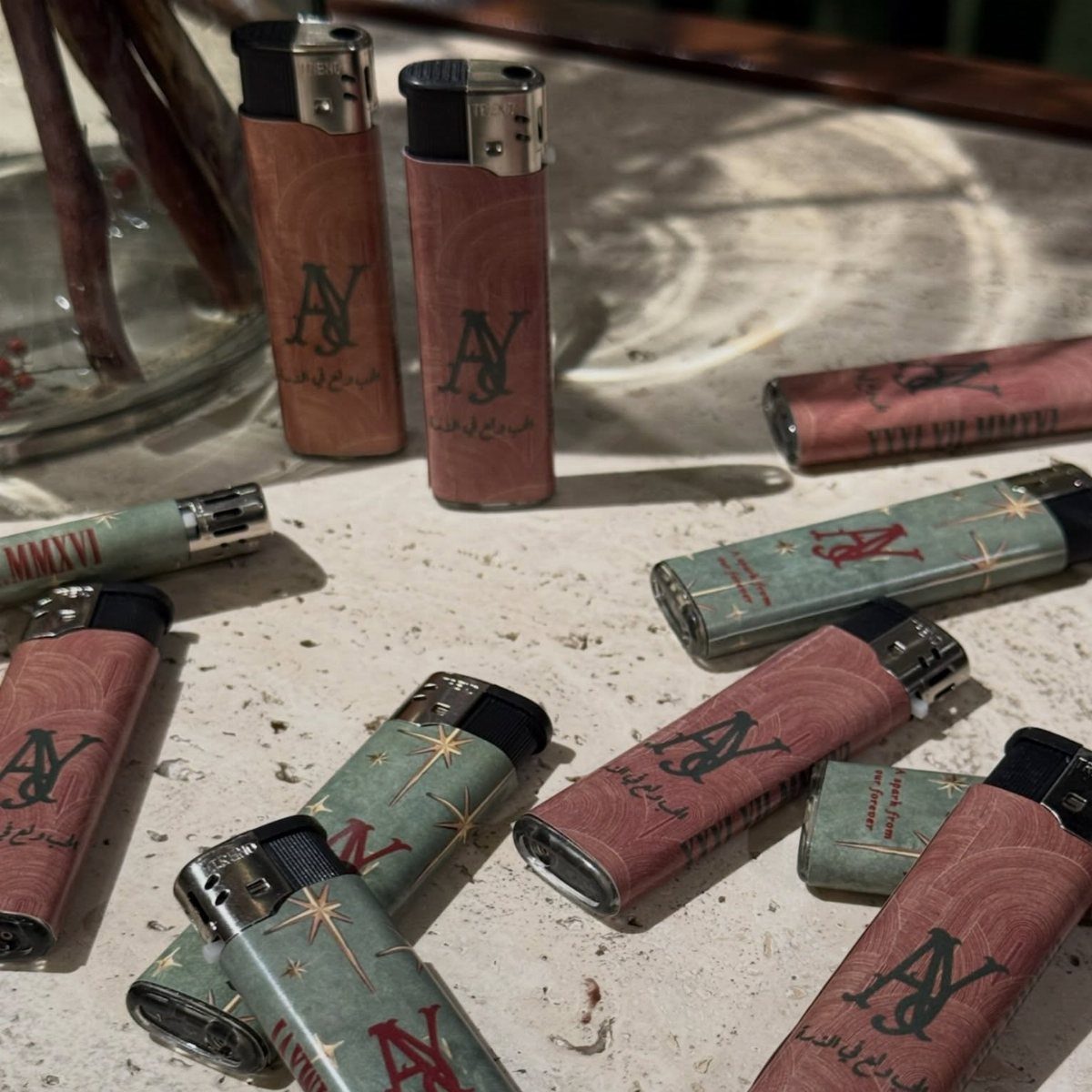 Monogrammed lighters in red and teal scattered on a light stone surface.