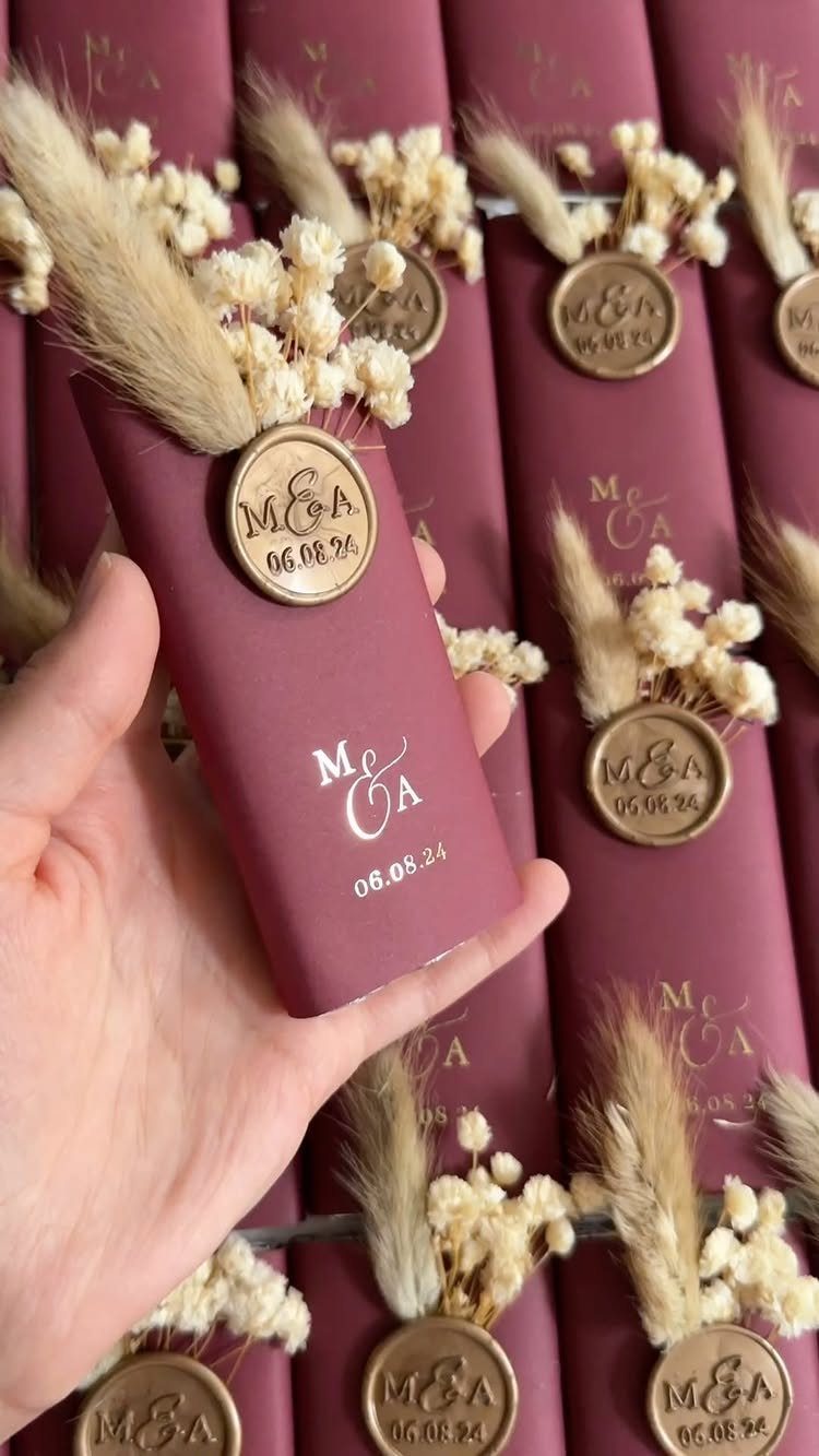 Burgundy matchbox wedding favor with gold wax seal and dried white flowers.