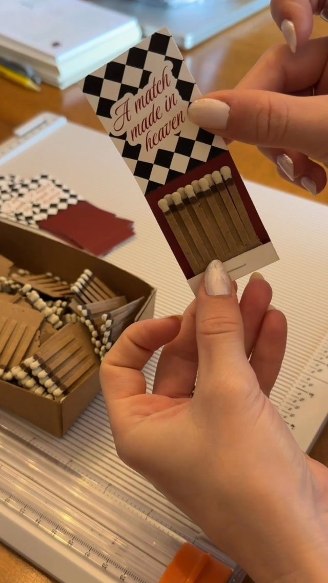 Hands holding a checkered wedding matchbox favor that says A match made in heaven