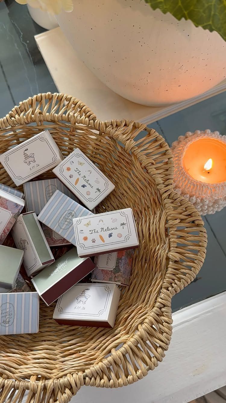 Customized matchboxes in a woven wicker bowl next to a lit white candle.