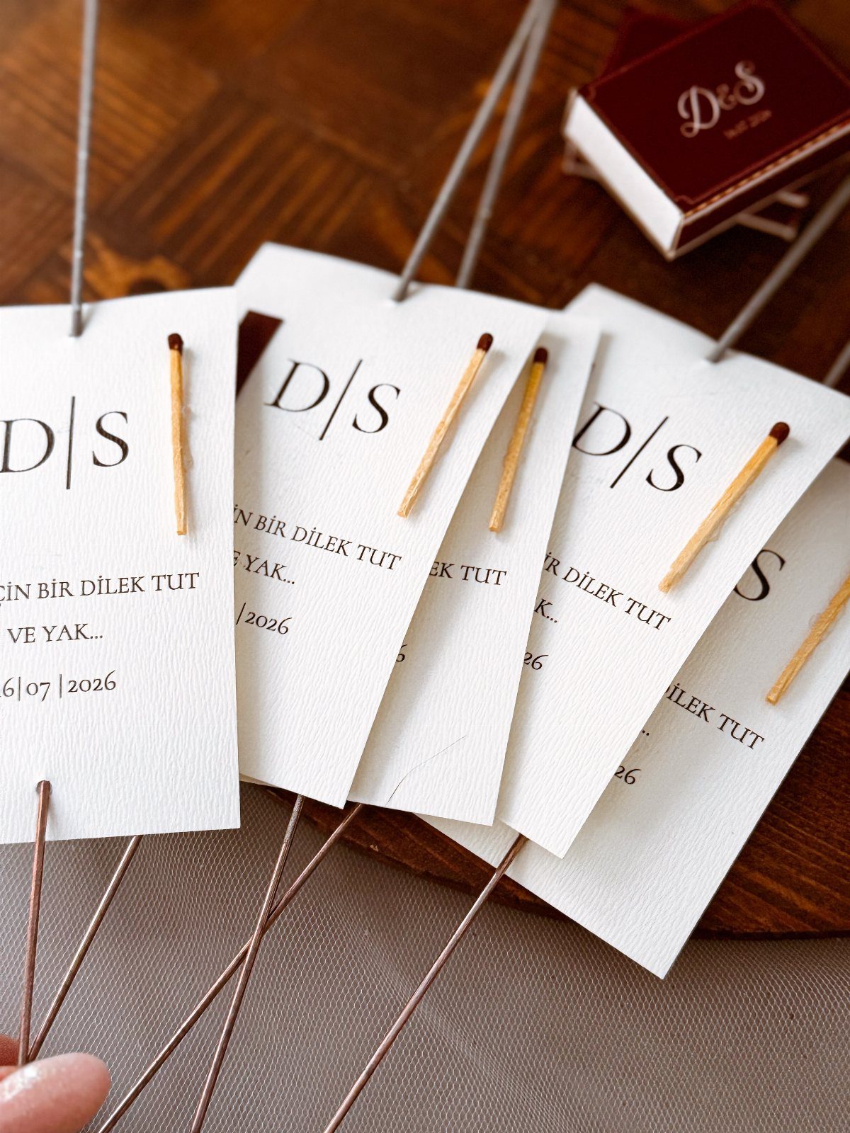 White wedding favor cards with attached matchsticks and initials on wooden surface