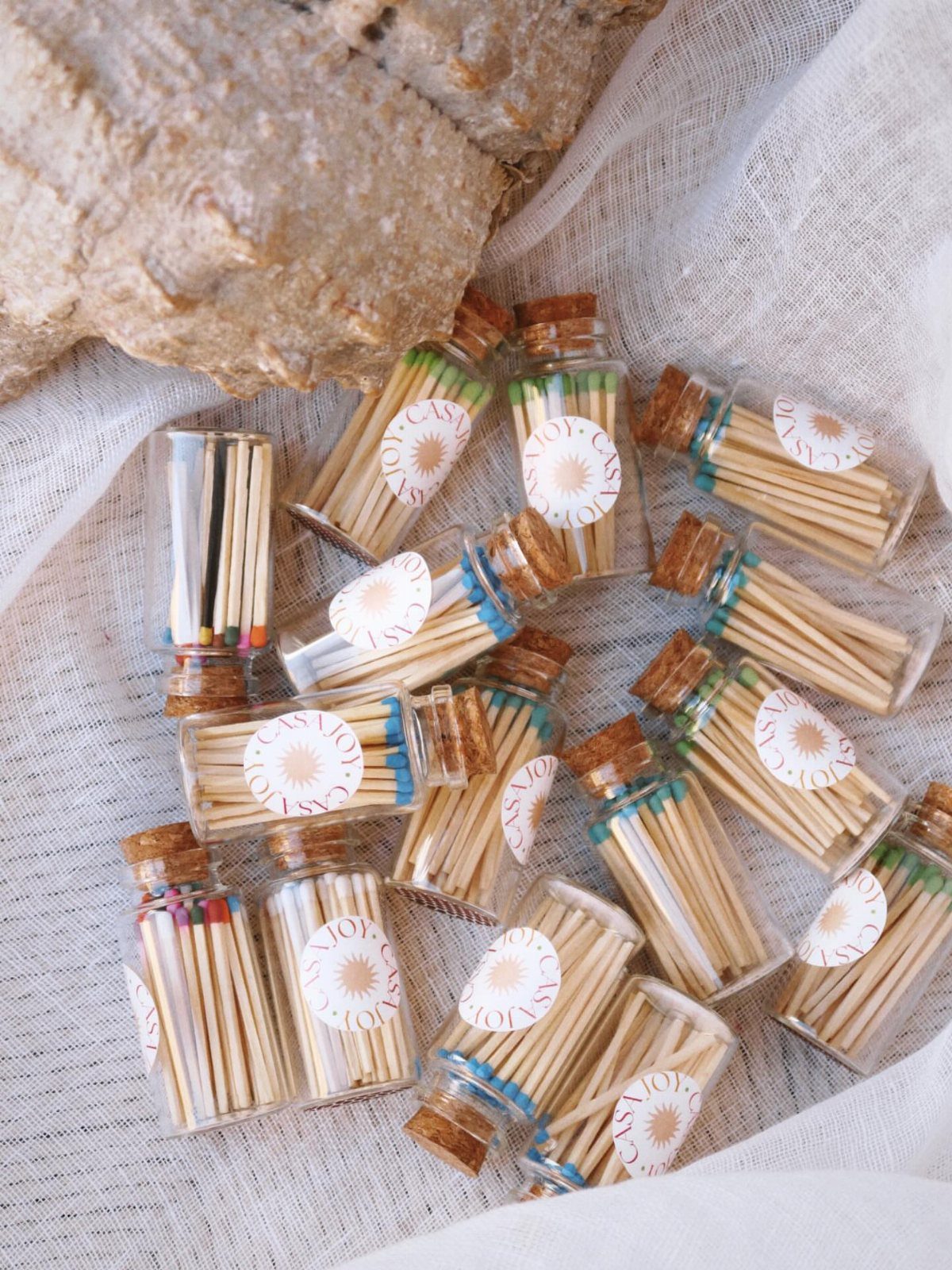 Small glass vials filled with wooden matches and floral labels on white fabric.