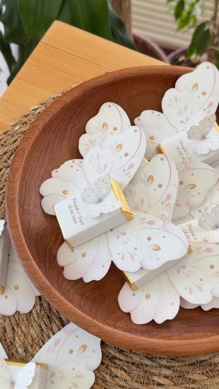 Butterfly-shaped wedding matchbox favors resting in a brown wooden bowl.