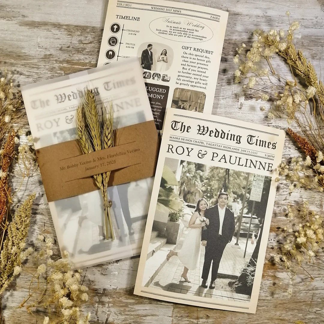 Newspaper wedding invitations with a couple's photo and dried wheat on wooden background