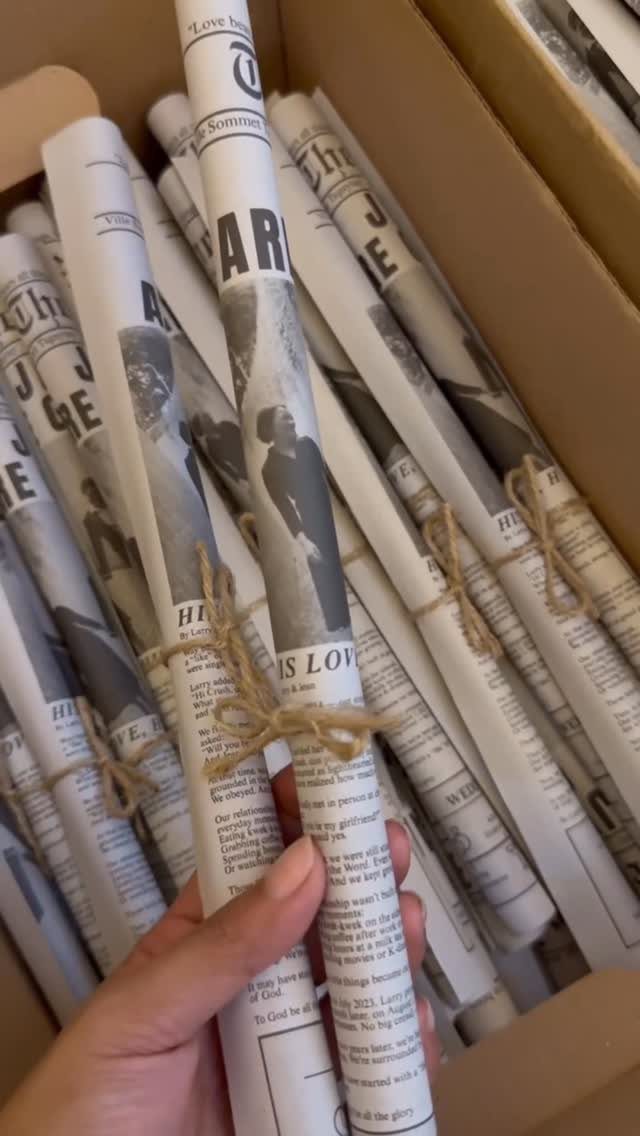 Rolled wedding newspapers tied with twine inside a brown cardboard shipping box.