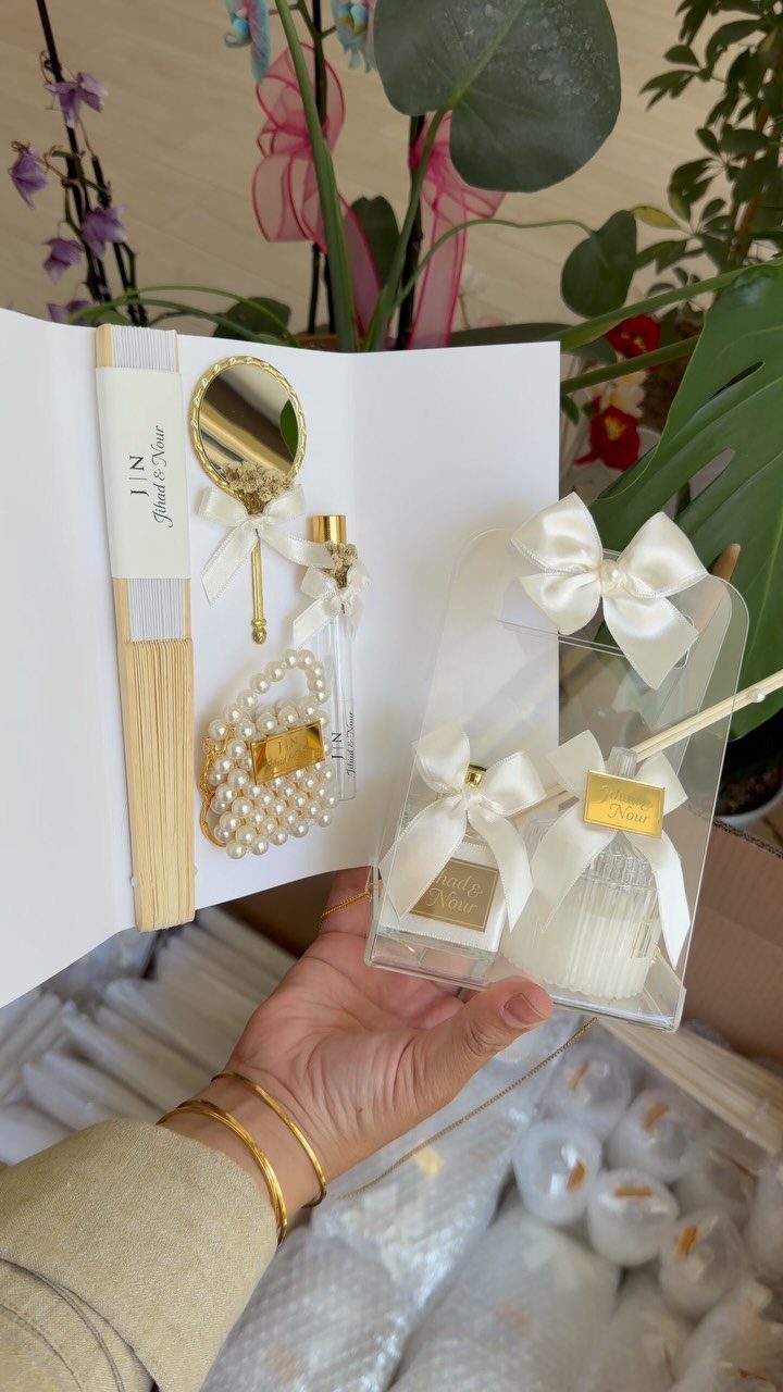 Gift boxes containing a white candle, gold mirror, and pearl pouch for weddings.