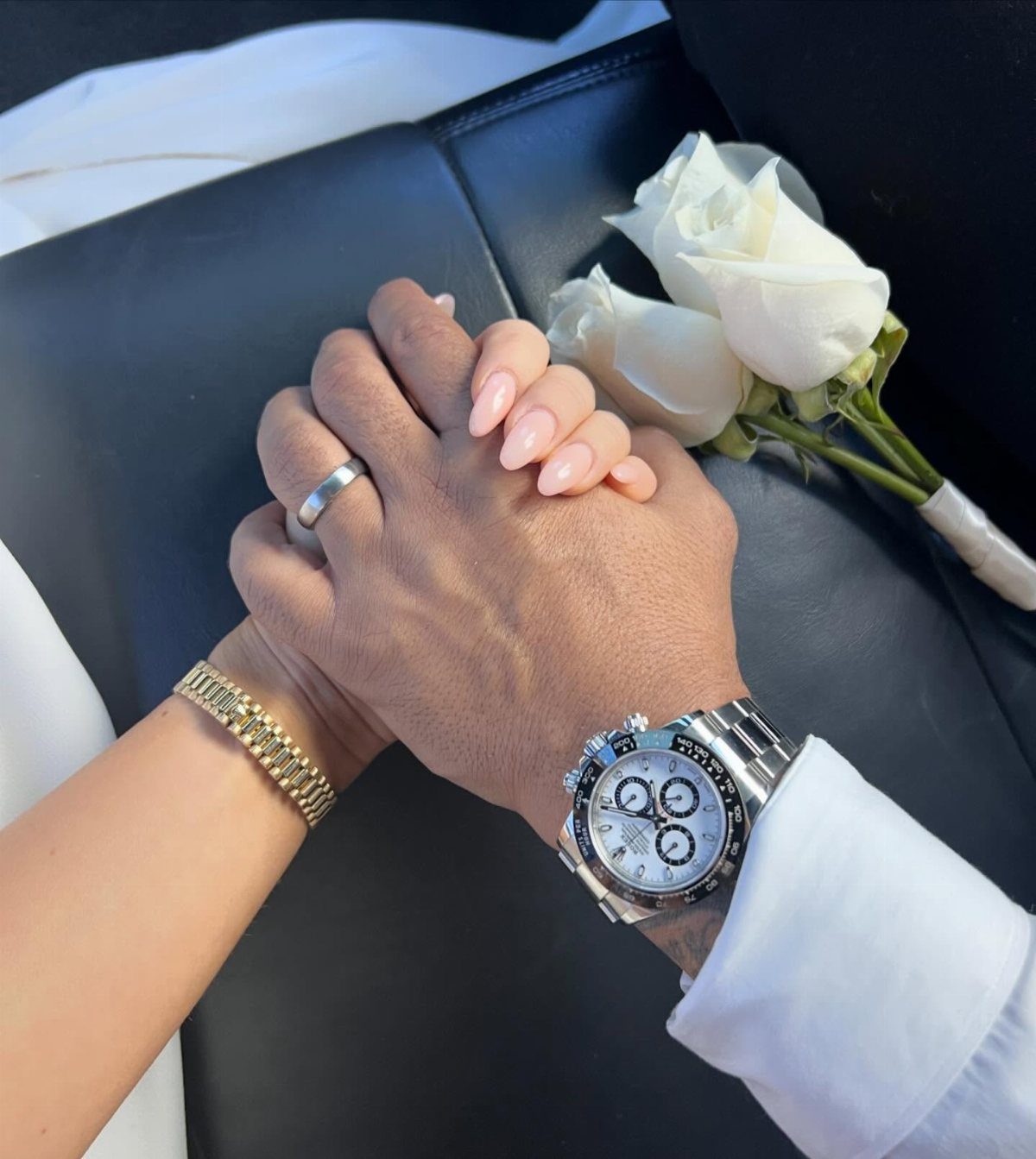 Couple holding hands featuring a silver luxury watch and white wedding roses
