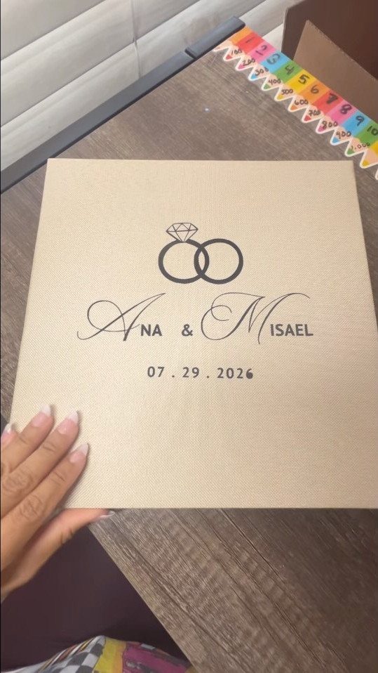 Beige fabric photo album with interlocking rings, names Ana and Misael, and wedding date.