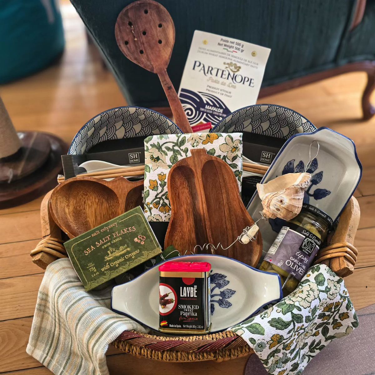 Gourmet cooking basket with pasta, spices, olives, wooden utensils, and ceramic dishes.