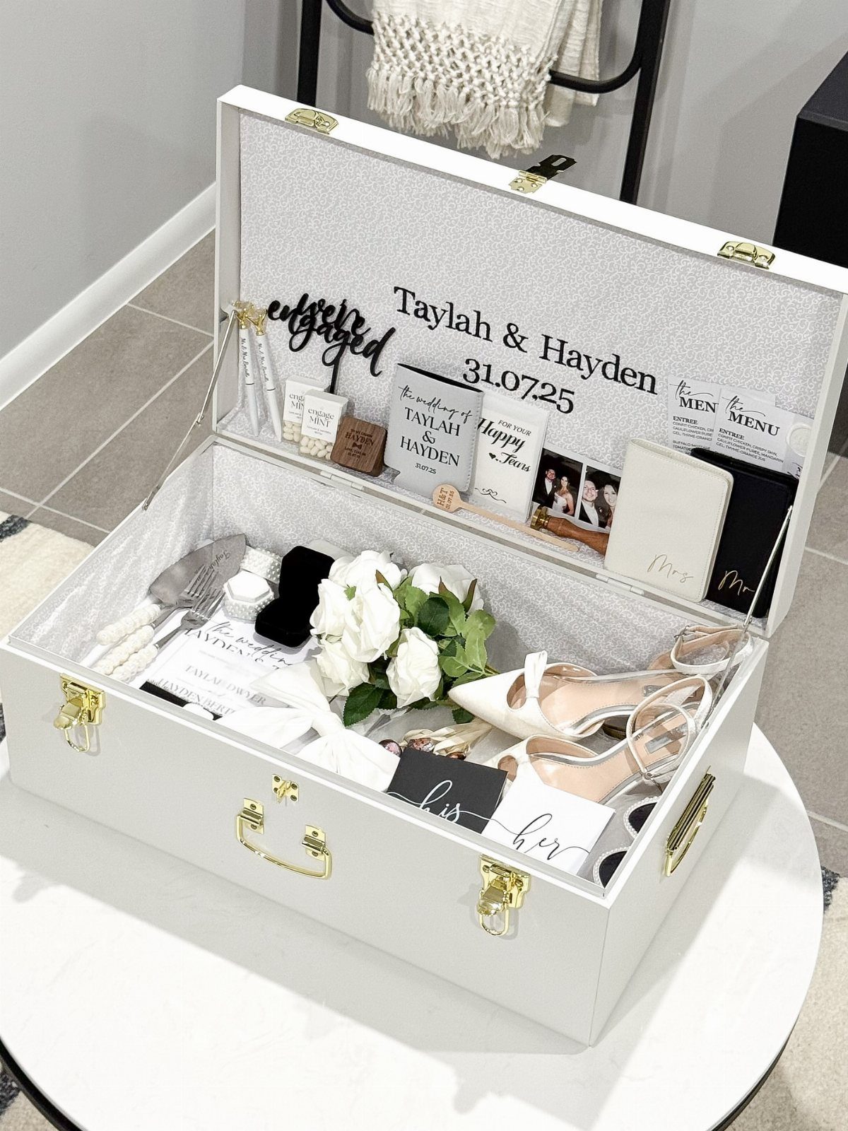 White keepsake box filled with wedding mementos, white shoes, and personalized stationery.