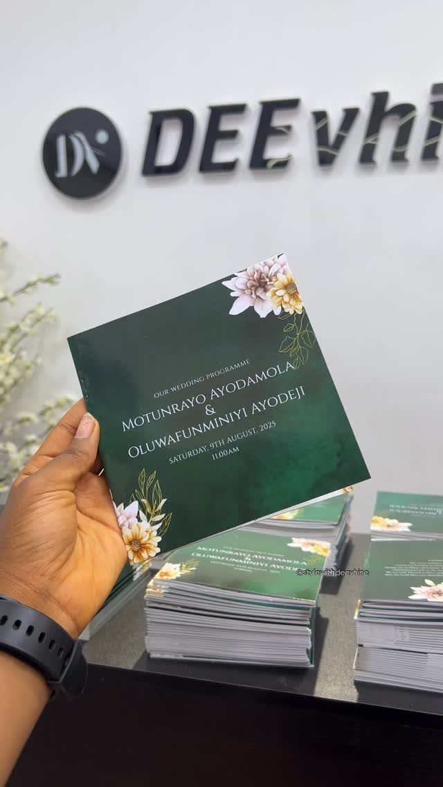 Dark green wedding program with floral designs held by a person's hand.
