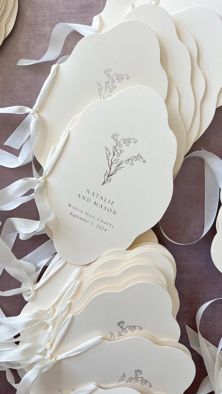 Cream-colored wedding programs with floral illustrations and ribbons on a purple background