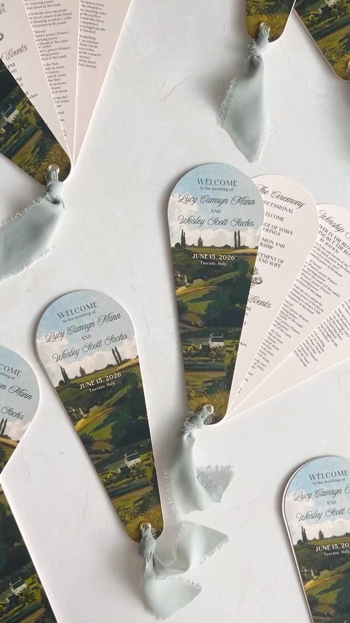 Fan-shaped wedding programs with landscape imagery and blue velvet ribbon ties.