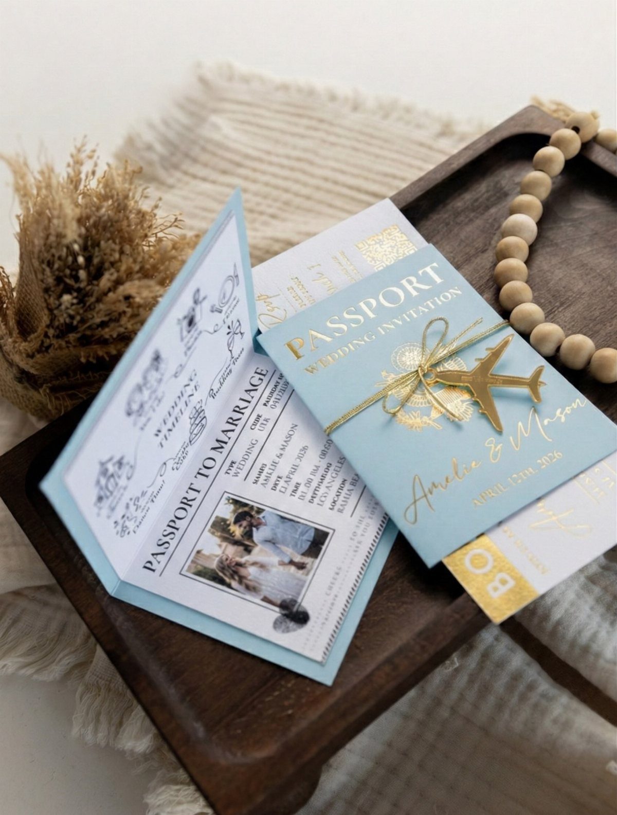 Passport-style wedding invitation and program with gold foil accents on a wooden tray