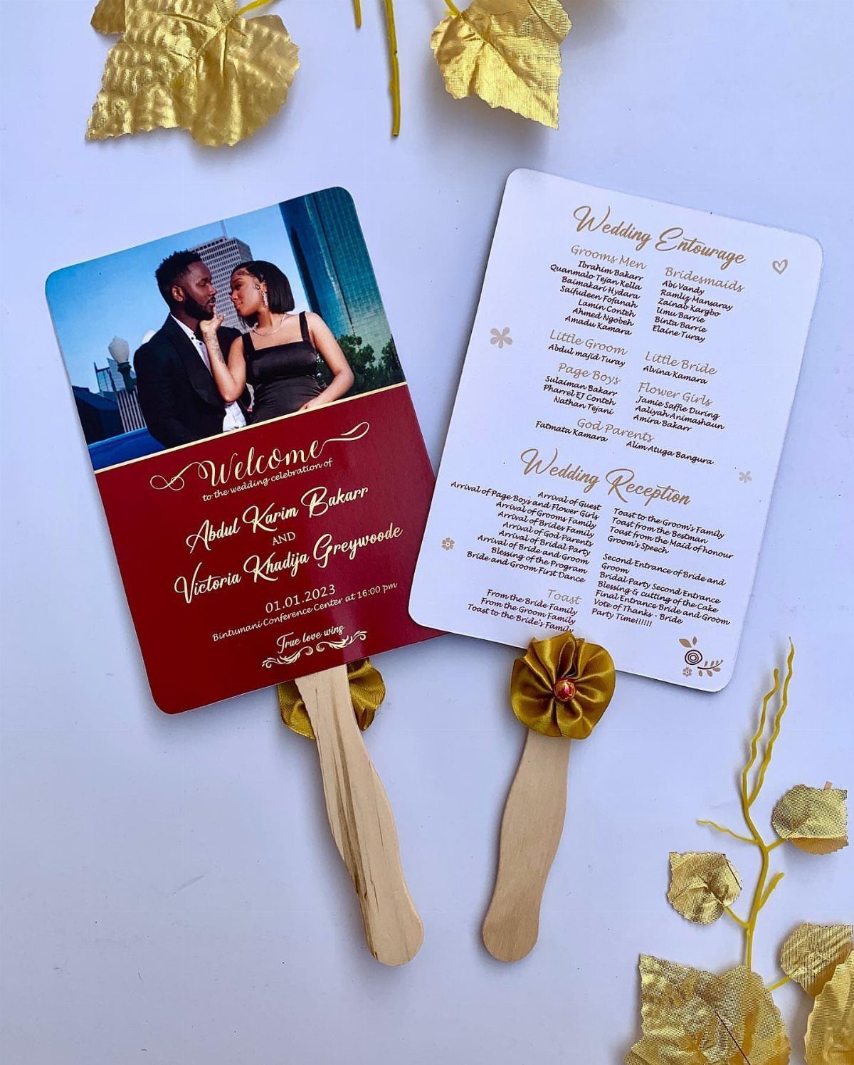 Two paddle-style wedding program fans with wooden handles and gold leaf accents.