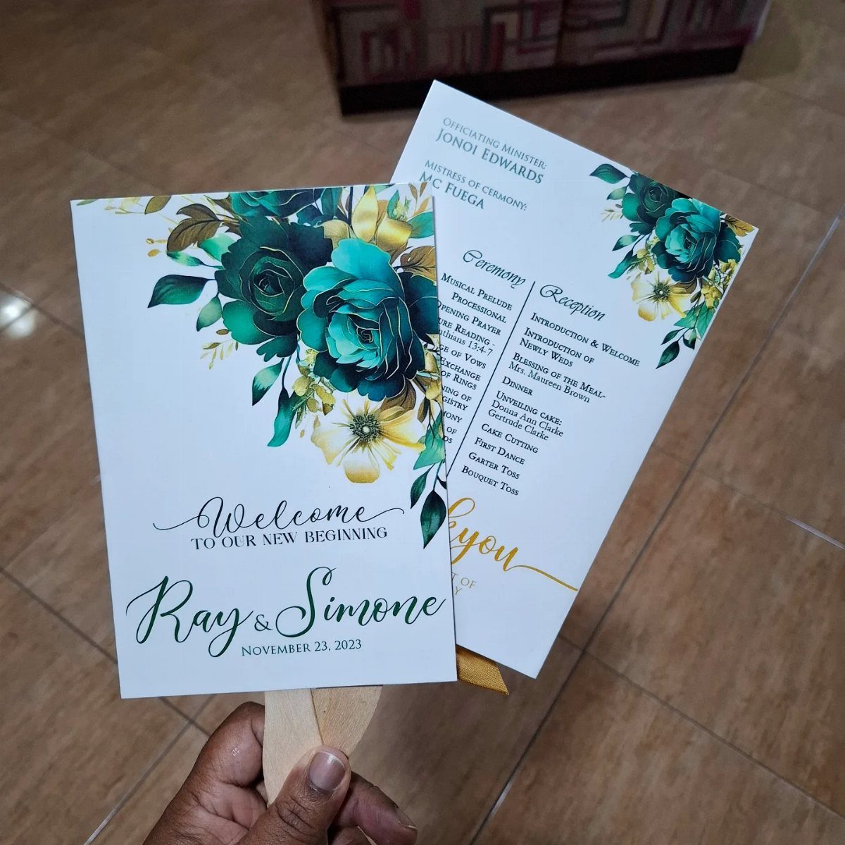 Wedding program fans with teal floral illustrations and elegant script on white cardstock.