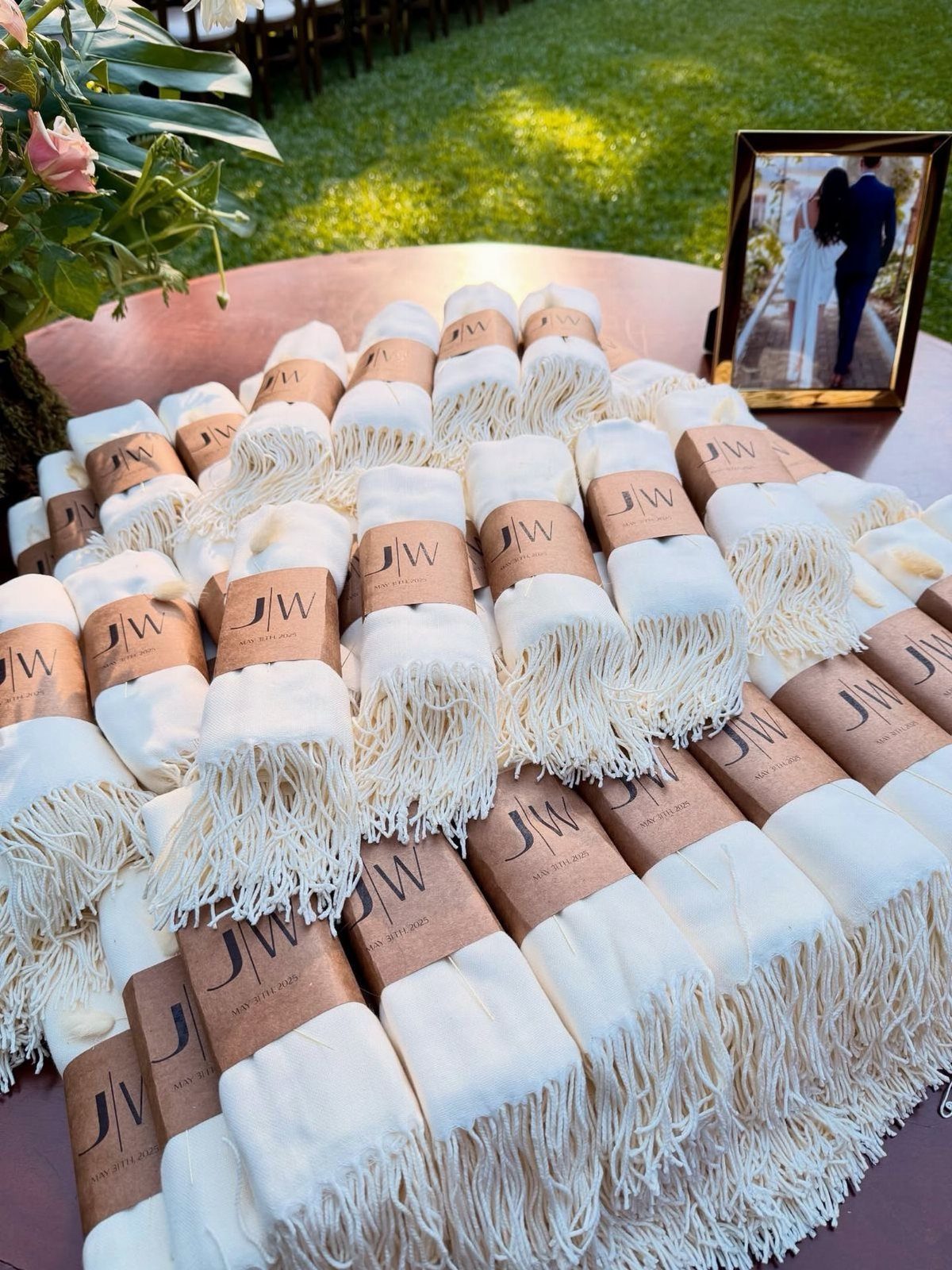 White fringed shawls rolled and tied with personalized brown paper bands on a table.