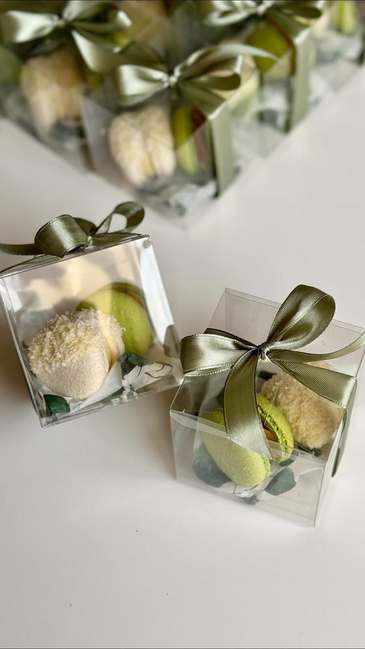 Macarons in clear gift boxes tied with olive green satin ribbons on white.