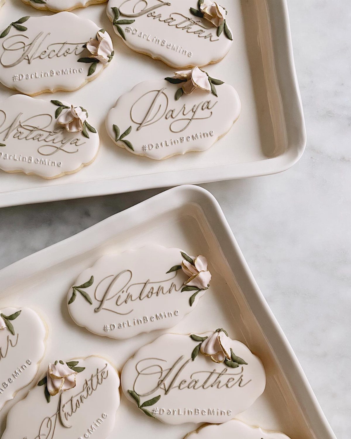 Custom iced sugar cookies with names and flowers on white serving trays.
