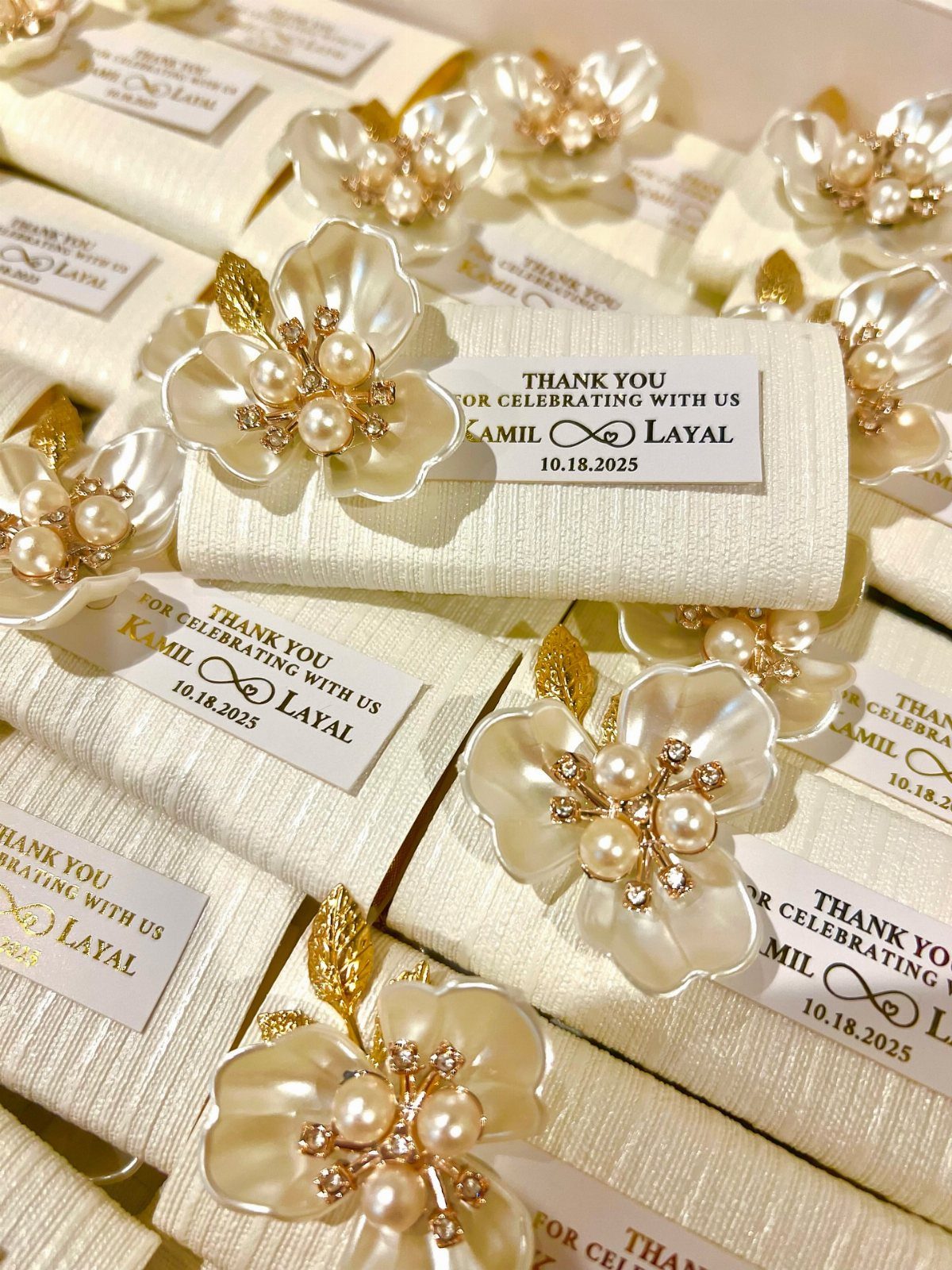 Cream fabric wedding favors with pearl flower brooches and personalized thank you tags.