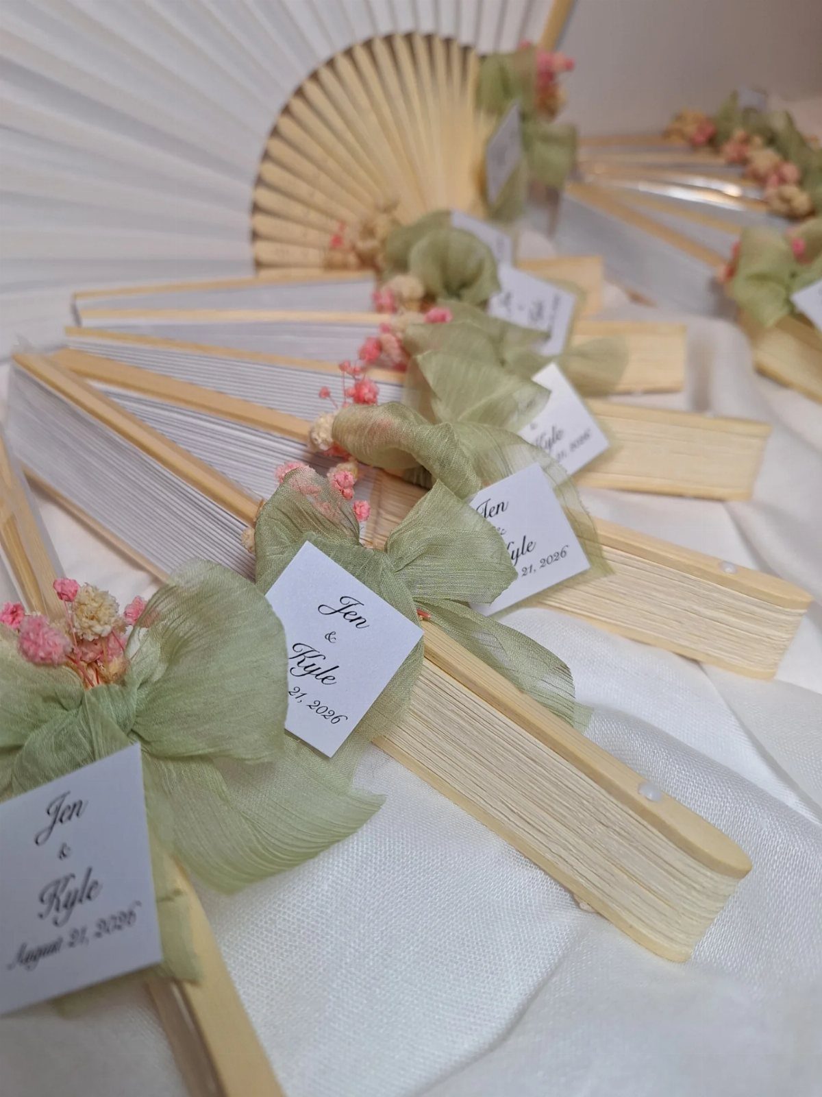 White hand fans with green ribbons and name tags for a wedding reception.