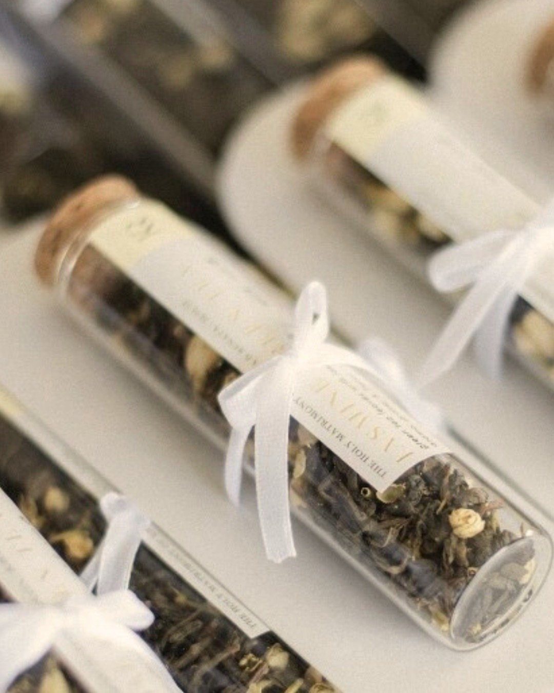 Glass test tubes filled with dried herbal tea, tied with white ribbons.