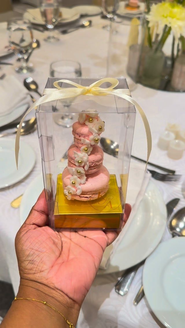 Small pink tiered cake with pearls in a clear gift box held by hand.