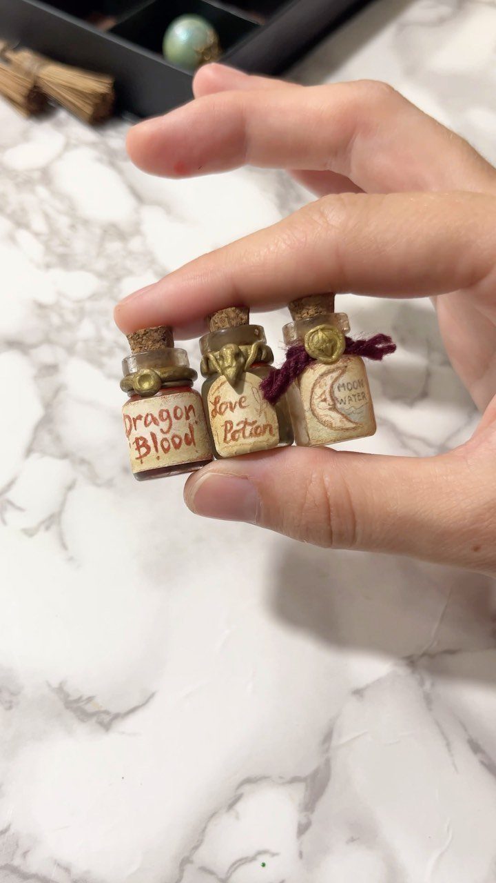 Three tiny potion bottles with aged labels held in a person's hand.