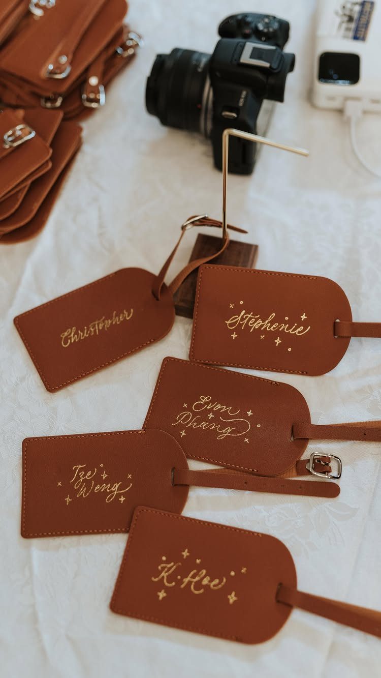 Brown leather luggage tags with gold foil names on a white cloth surface.