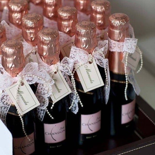 Mini champagne bottles decorated with white lace, pearls, and personalized name tags.