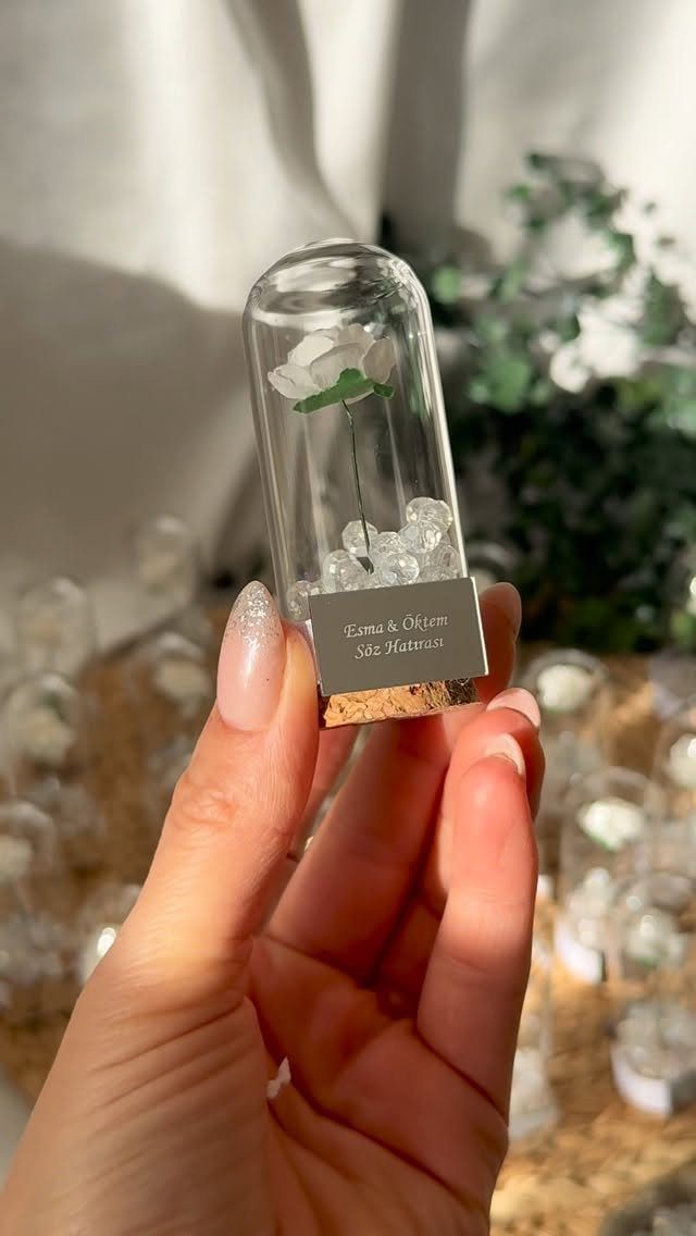 Small glass vial with a white flower and pebbles held in a hand
