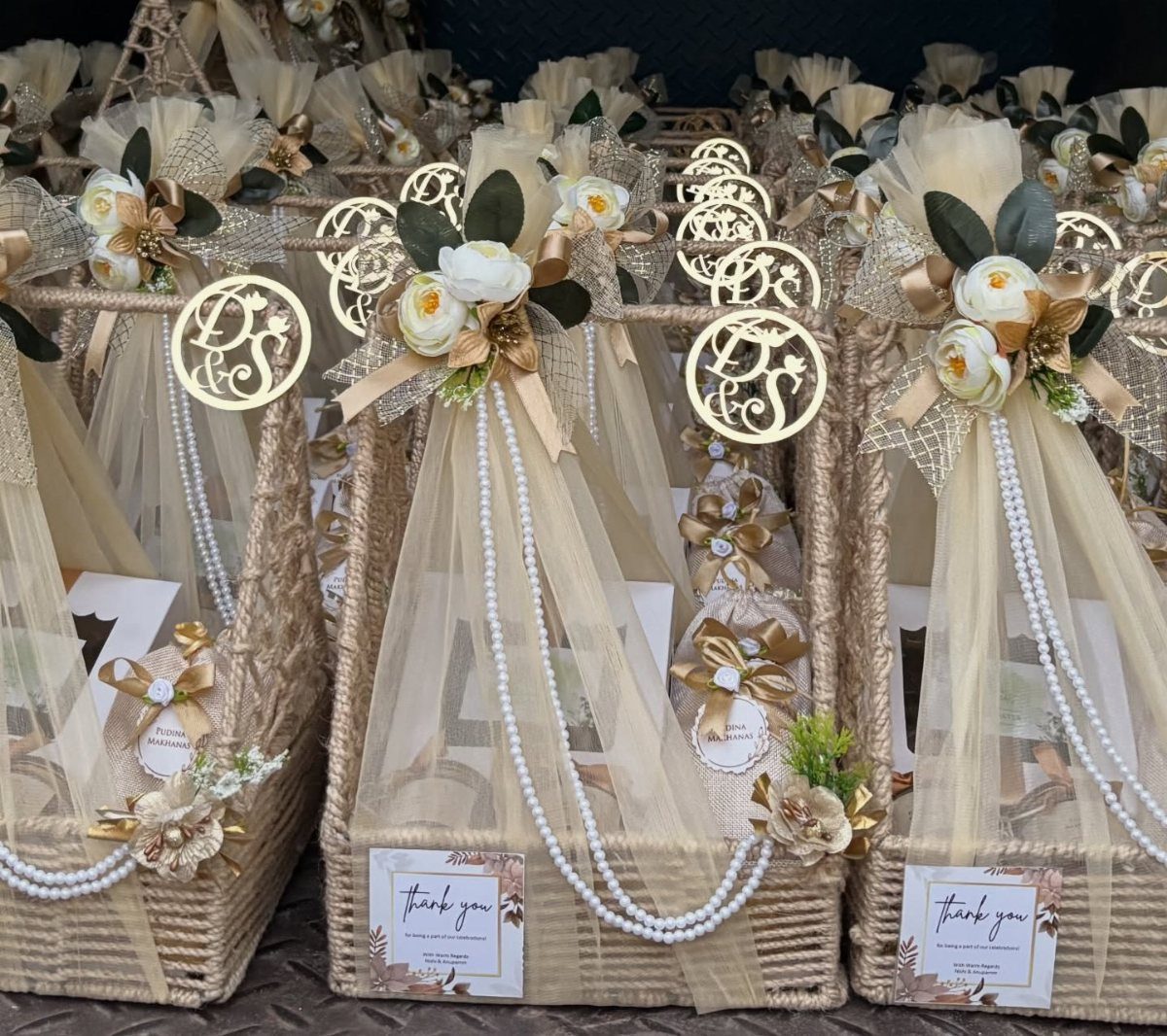 Woven gift baskets wrapped in beige tulle with white flowers and gold monograms.