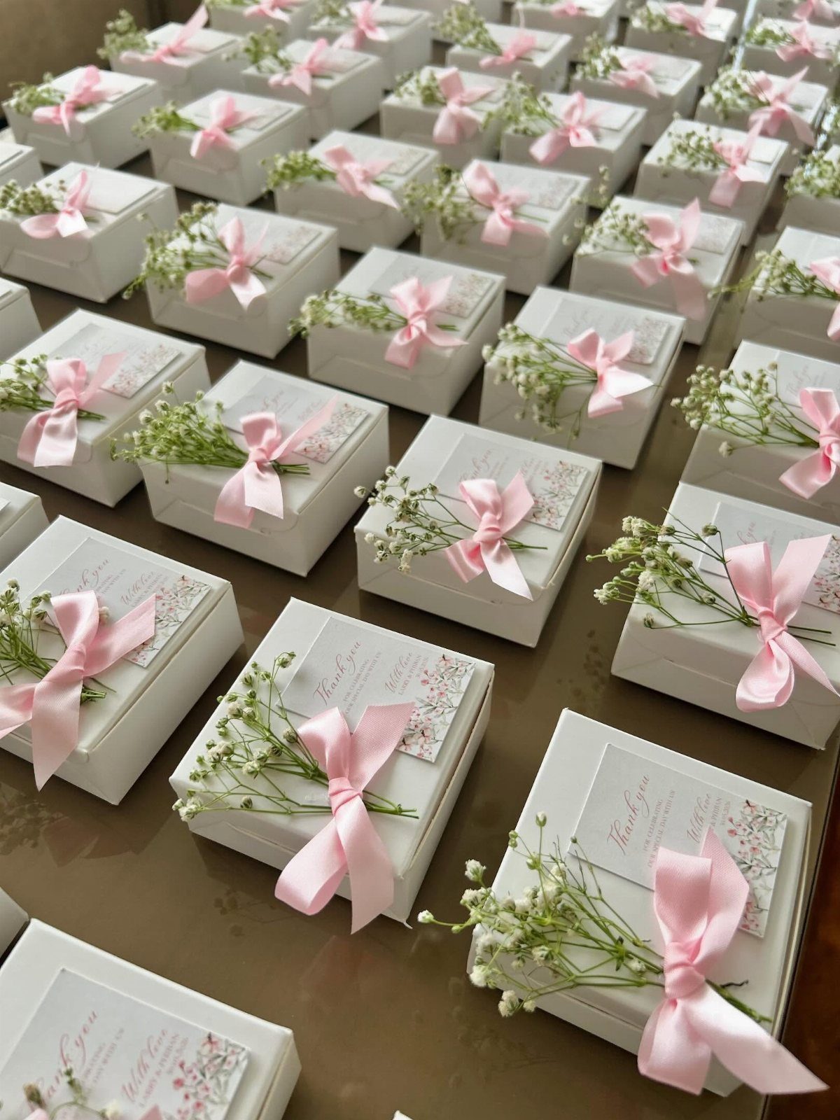 White square gift boxes with pink ribbons and baby's breath flowers for weddings.