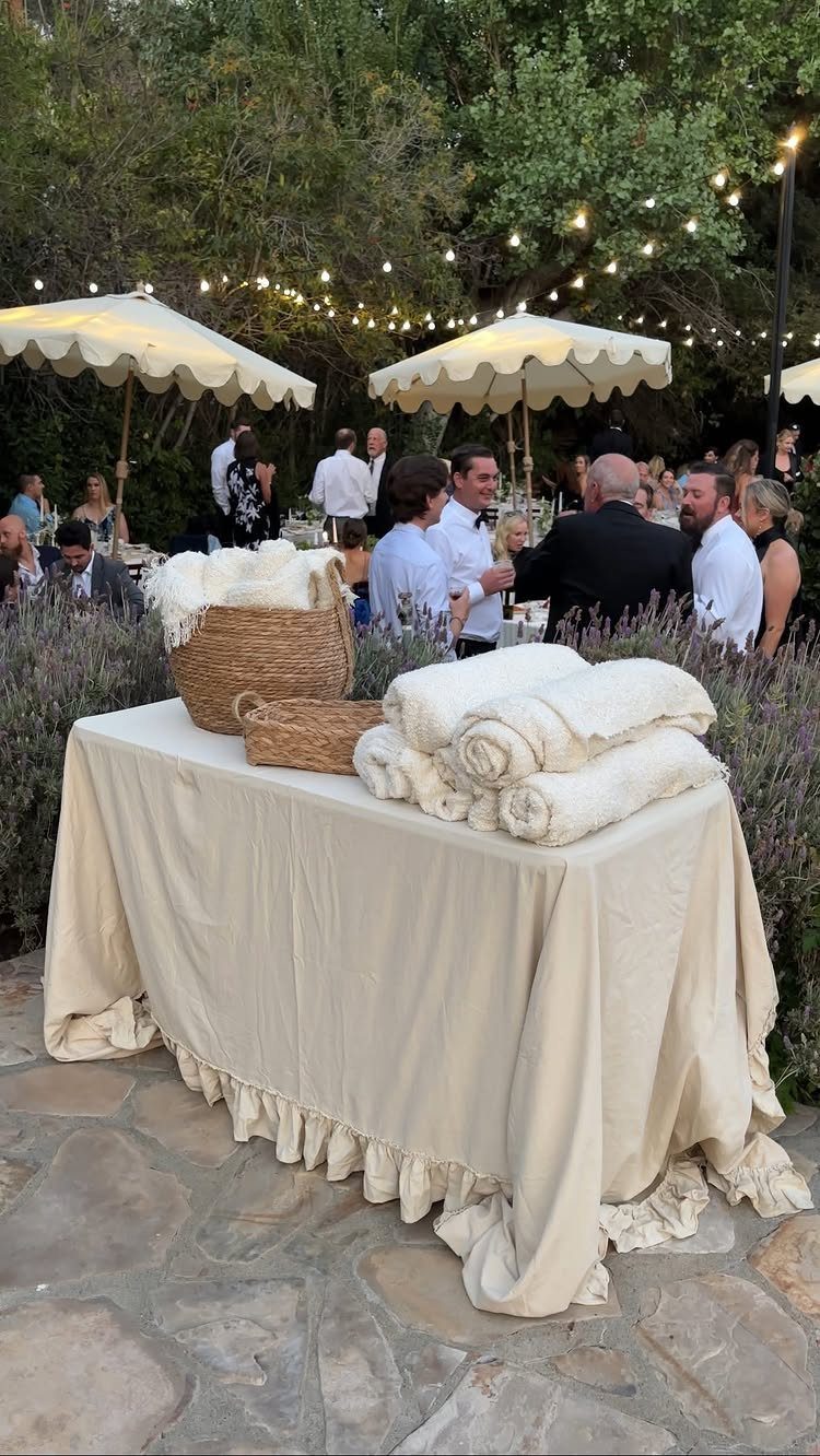 Rolled white towels in baskets on a draped table at an outdoor wedding.