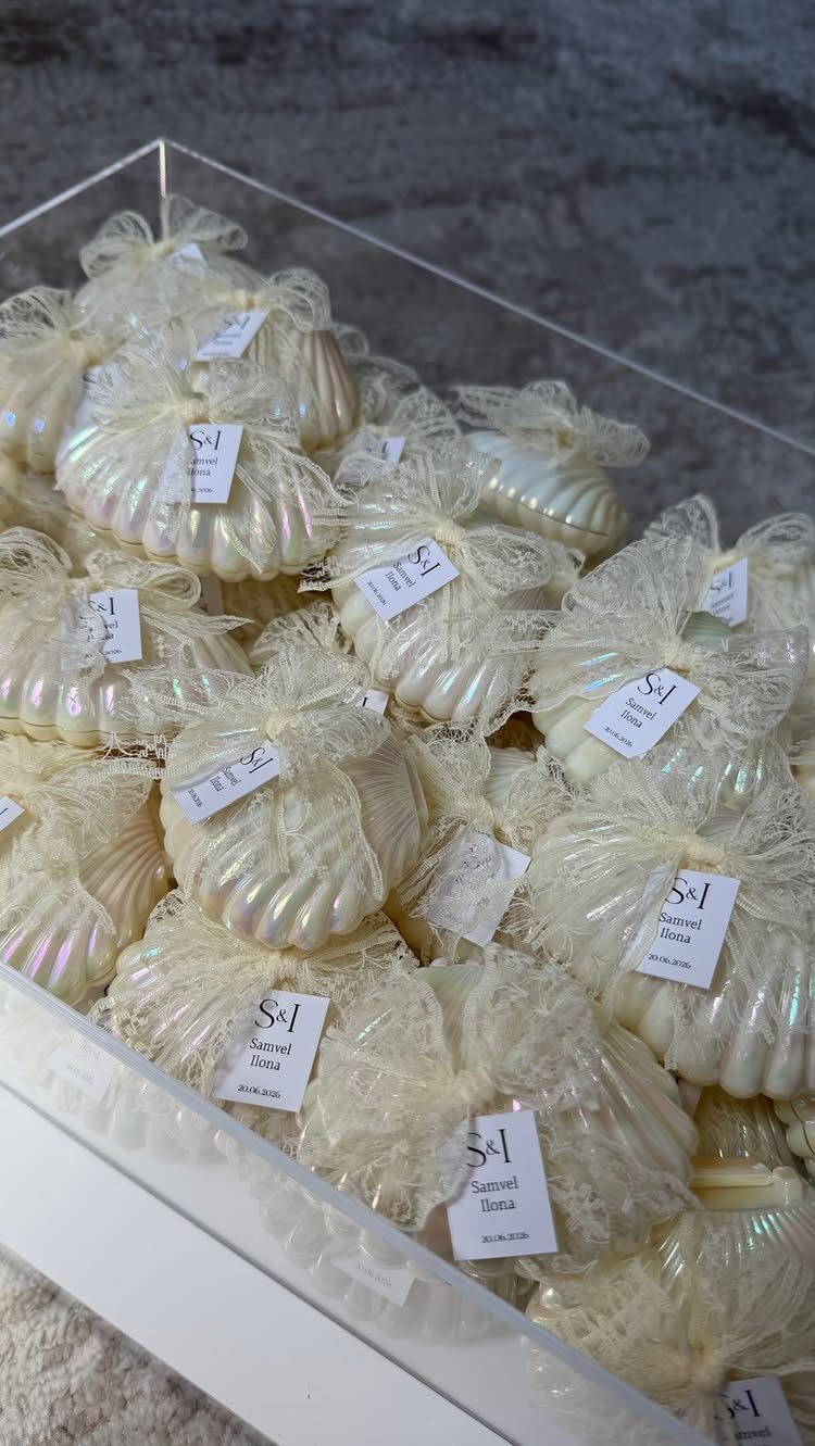 Iridescent shell-shaped soaps in white mesh bags with tags in a clear tray.