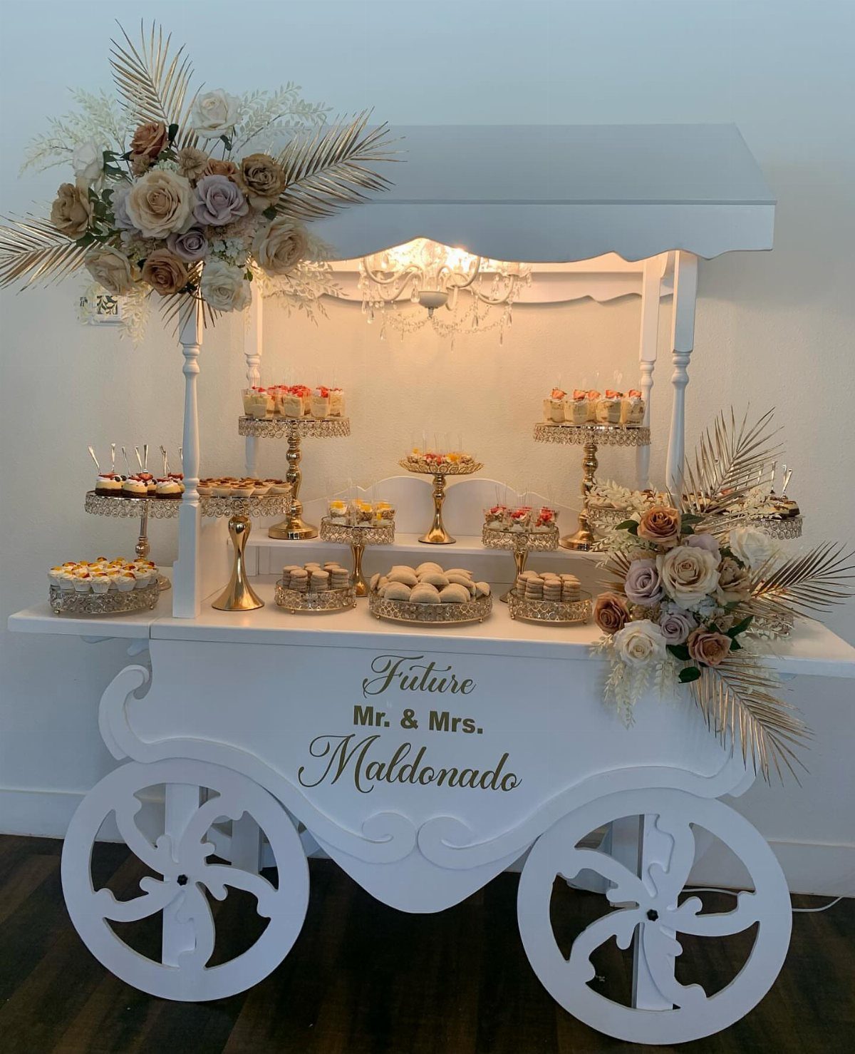 White dessert carriage cart filled with sweets and pastries for a wedding reception.