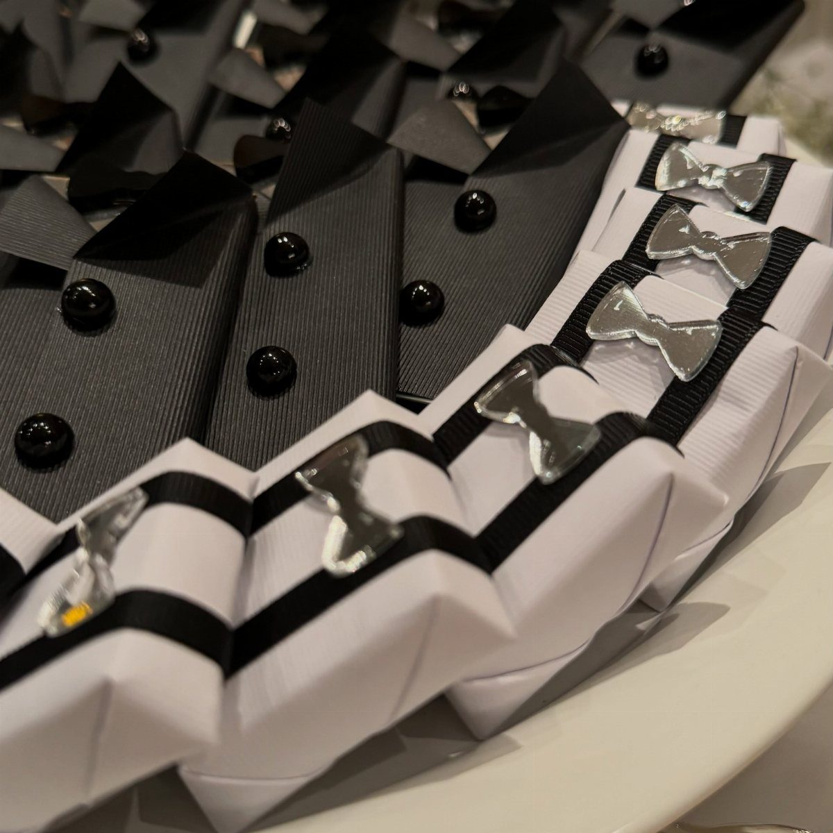 Tuxedo-themed wedding favor boxes in black and white with silver bow ties.