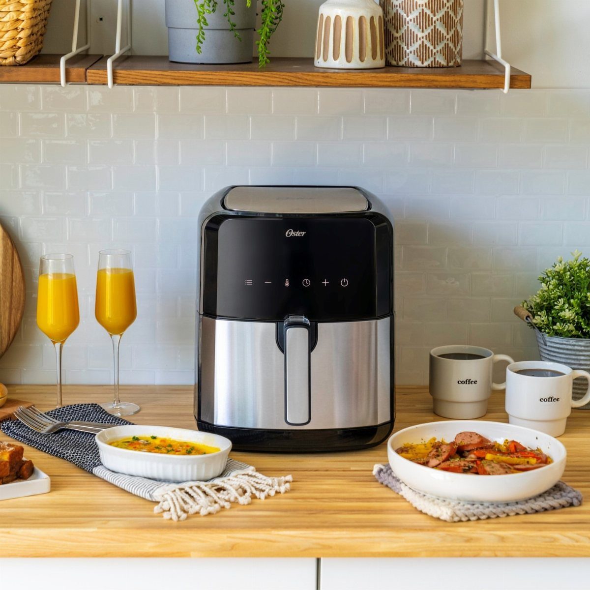 Oster air fryer on a wooden counter with orange juice and cooked meals.