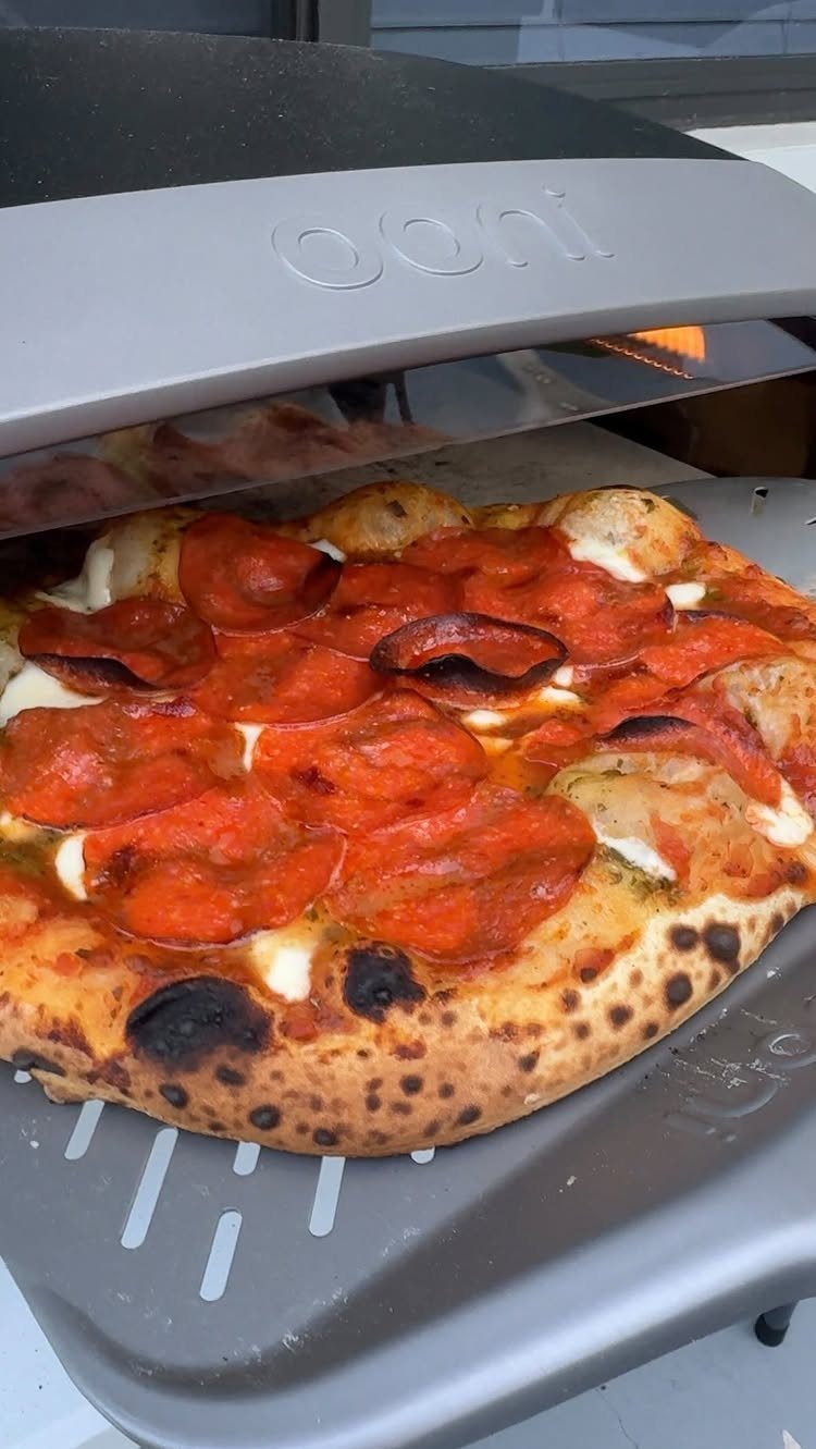 Pepperoni pizza with charred crust inside a grey portable pizza oven.