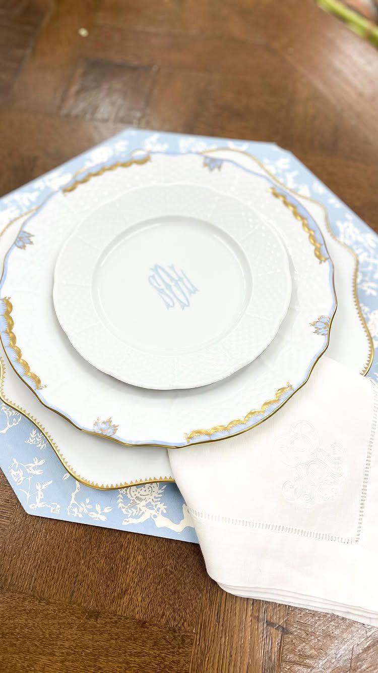 White ceramic plates with gold trim and blue monogram on a patterned placemat.