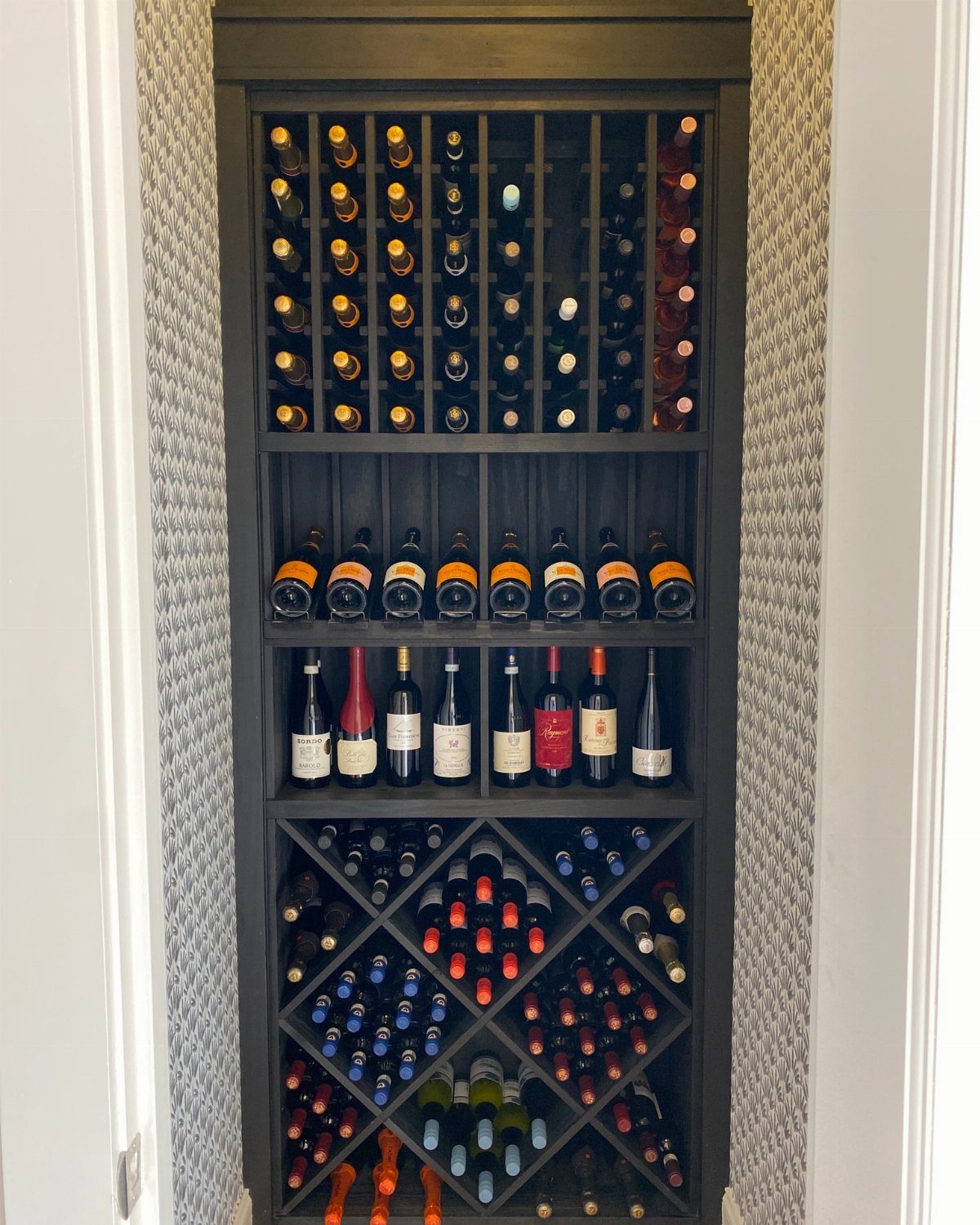 Dark wood built-in wine rack filled with various wine bottles in a home.