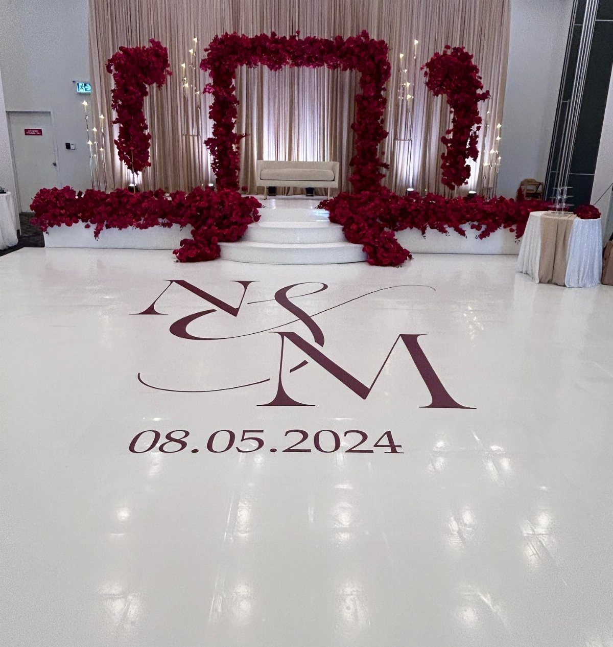 White glossy dance floor with maroon monogram and date, red floral backdrop.