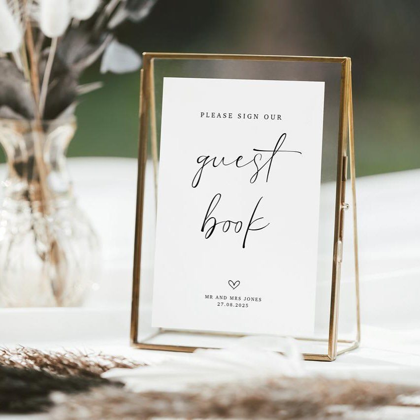 Guest book sign in a gold glass frame on a white wedding table.