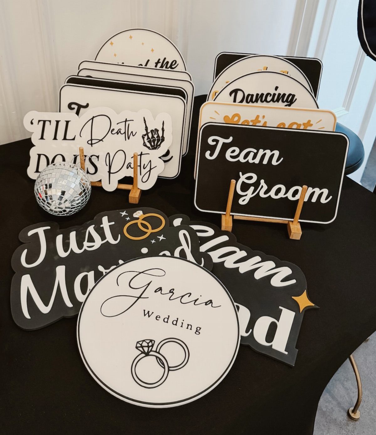 Wedding photo booth props and signs with gold accents on a black table.