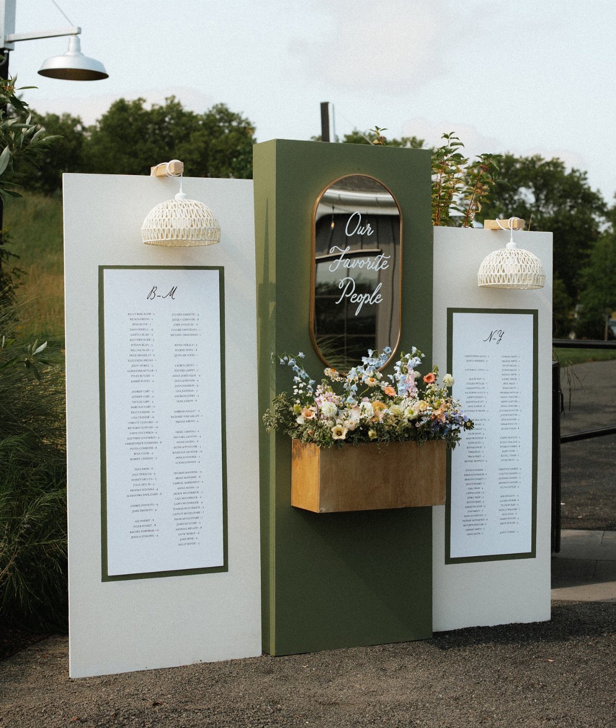 Wedding seating chart with white and green panels, a mirror, and floral arrangements.