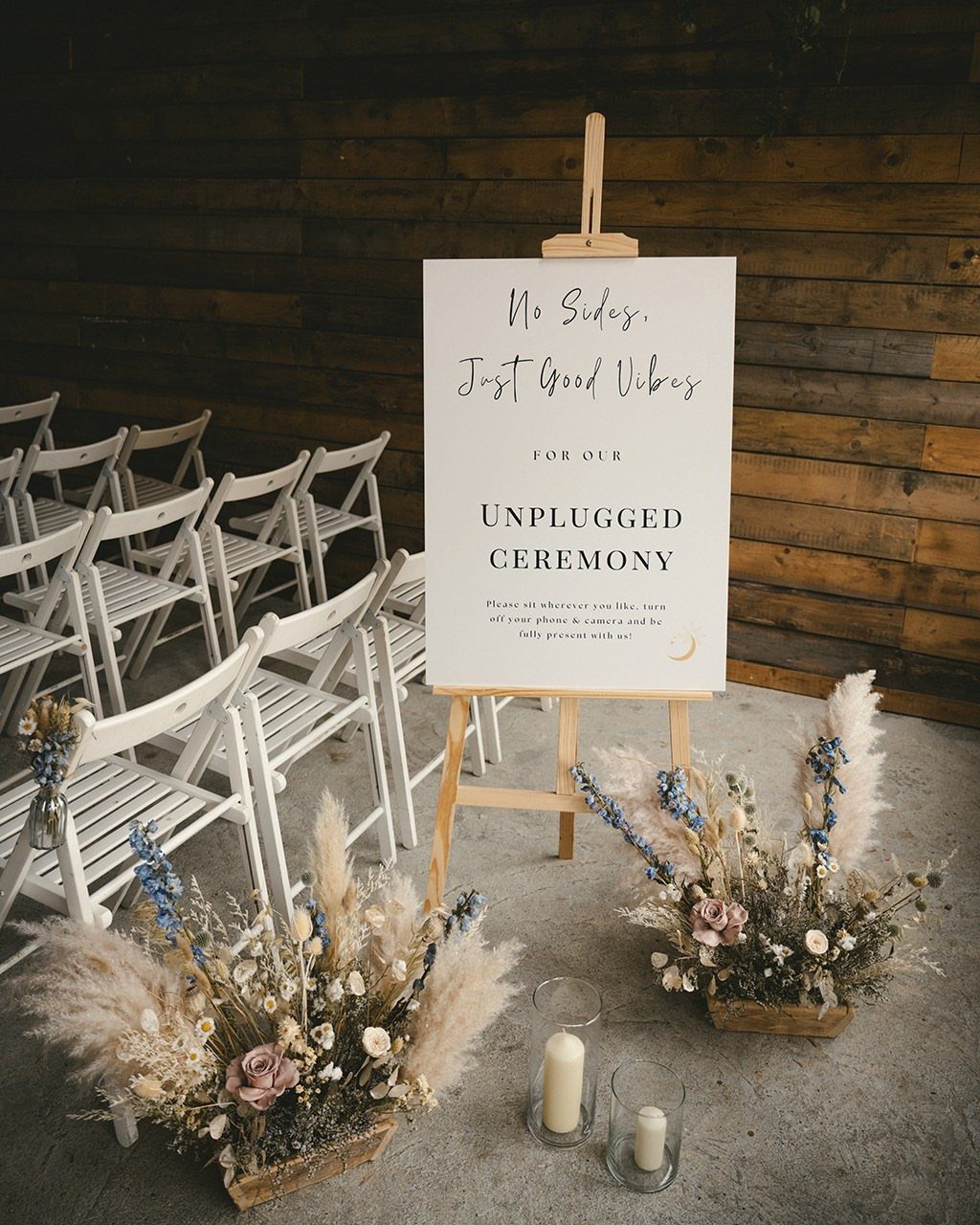 Unplugged ceremony sign on a wooden easel with white chairs and floral arrangements.