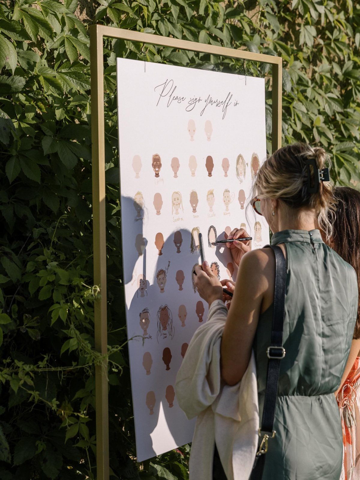 Woman coloring a face on an interactive guestbook sign in a gold frame.