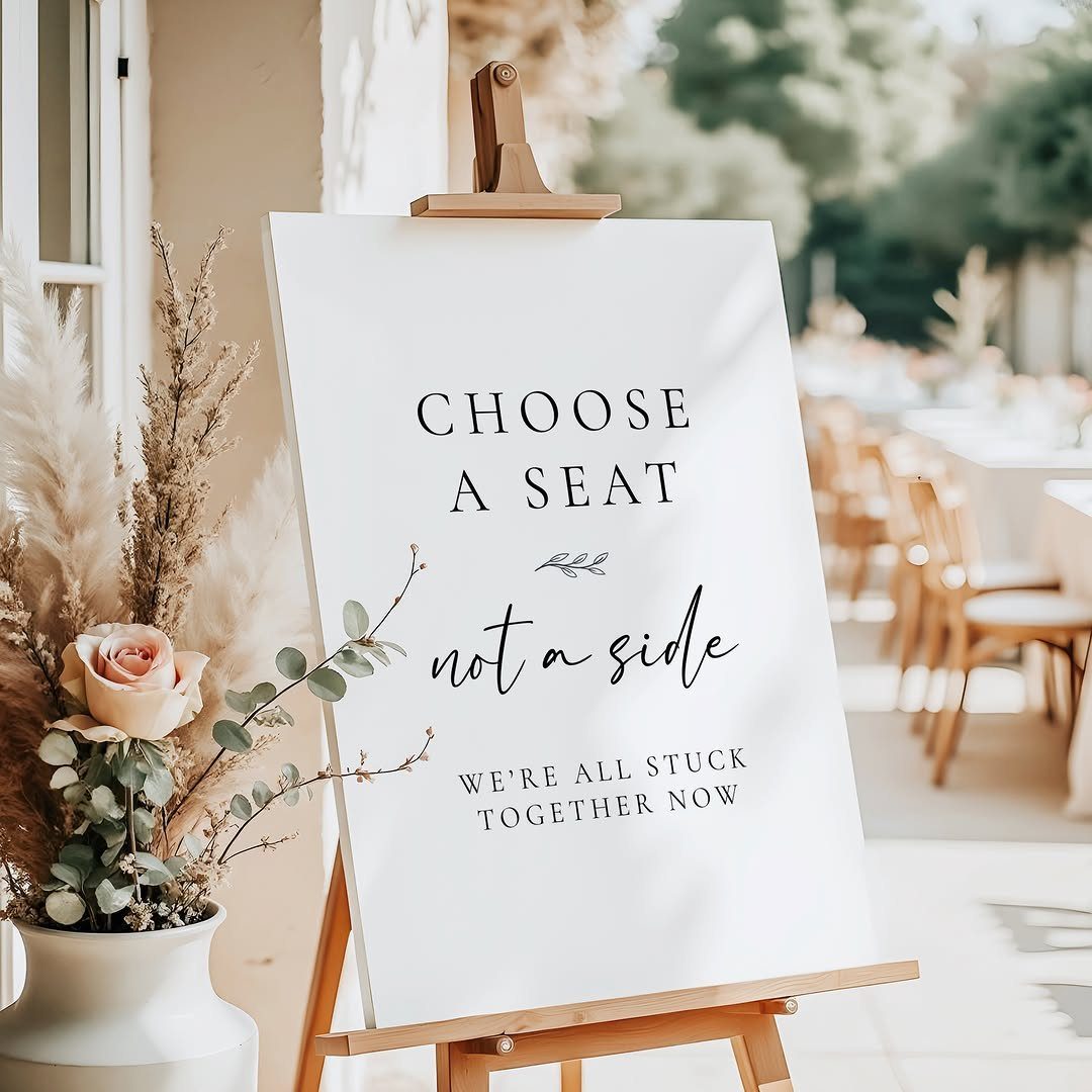 White wedding sign on wooden easel saying choose a seat not a side